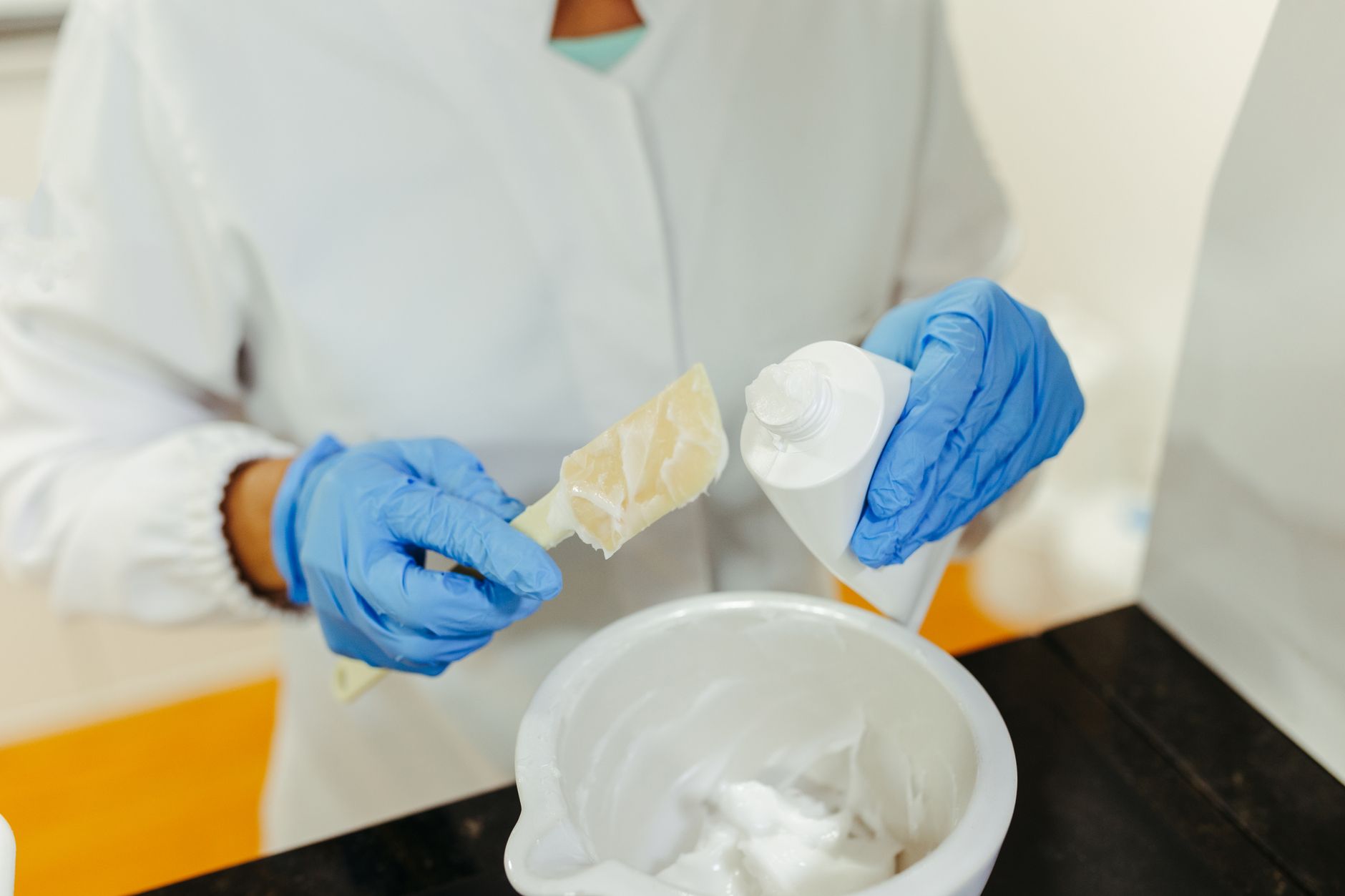 Técnica de laboratório usando luvas mistura um creme para cuidados com a pele durante um procedimento de pesquisa.