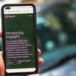 Pessoa segura um smartphone que exibe a interface do ChatGPT em uma página da OpenAI.