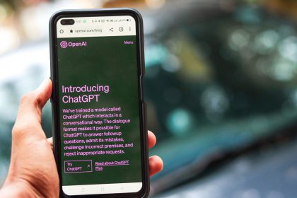 Pessoa segura um smartphone que exibe a interface do ChatGPT em uma página da OpenAI.