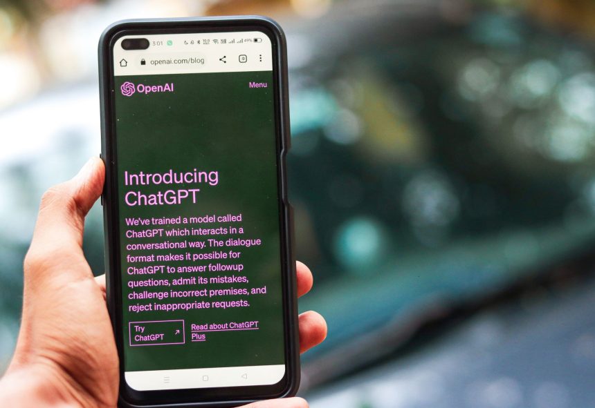 Pessoa segura um smartphone que exibe a interface do ChatGPT em uma página da OpenAI.