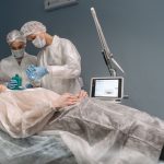 Dois médicos realizam um procedimento estético em uma paciente dentro de uma clínica.