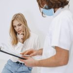 Profissional de saúde usando máscara conversa com uma paciente durante uma consulta em uma clínica.