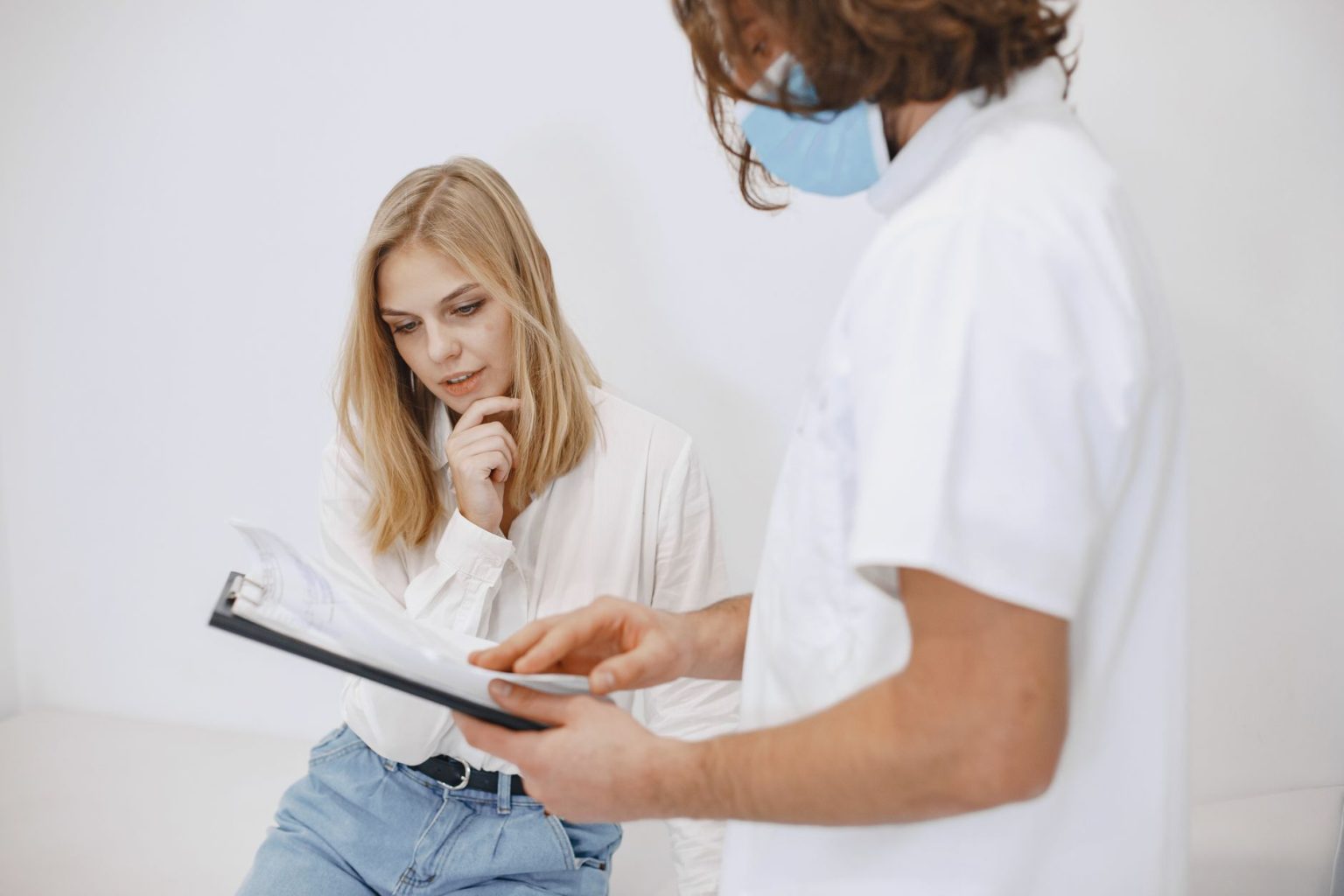 Profissional de saúde usando máscara conversa com uma paciente durante uma consulta em uma clínica.