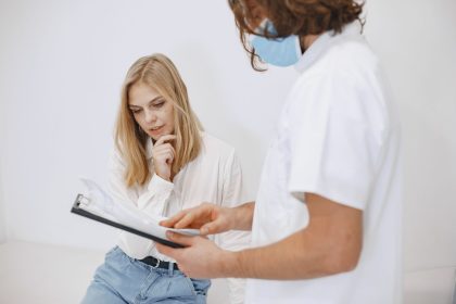 Profissional de saúde usando máscara conversa com uma paciente durante uma consulta em uma clínica.