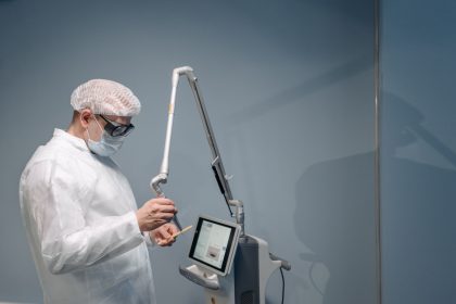 Médico utiliza equipamento de laser em procedimento dermatológico, usando proteção ocular, em ambiente clínico.
