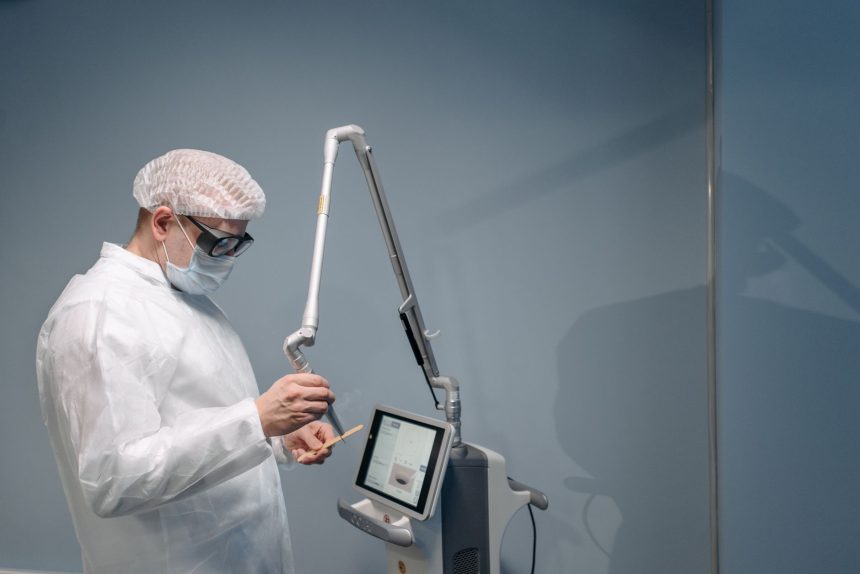 Médico utiliza equipamento de laser em procedimento dermatológico, usando proteção ocular, em ambiente clínico.
