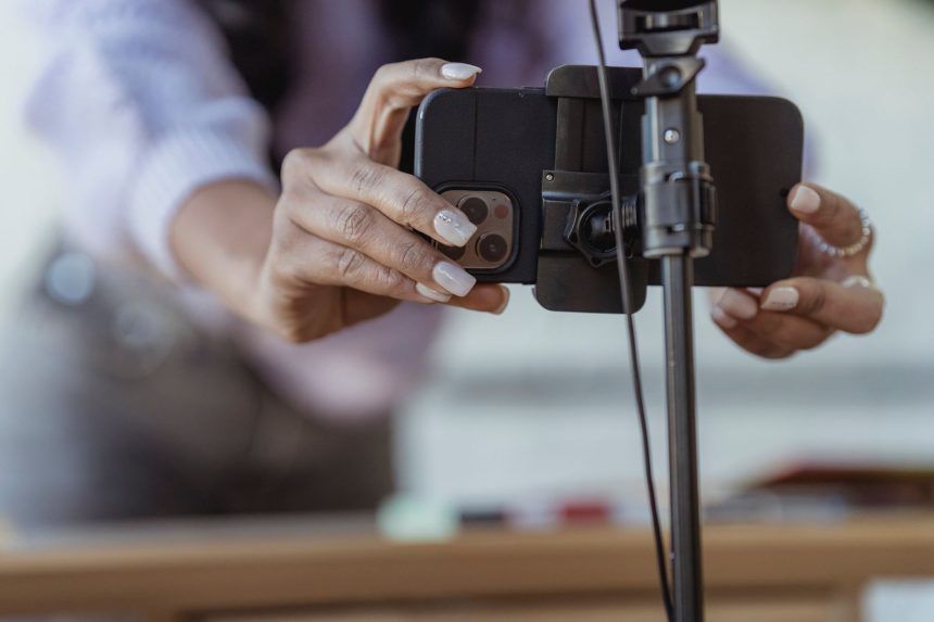 Pessoa posiciona um celular em um tripé para gravar um vídeo em ambiente interno.