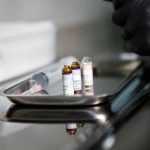 Frascos de produtos médicos e uma seringa sobre uma bandeja metálica em ambiente clínico