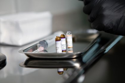 Frascos de produtos médicos e uma seringa sobre uma bandeja metálica em ambiente clínico