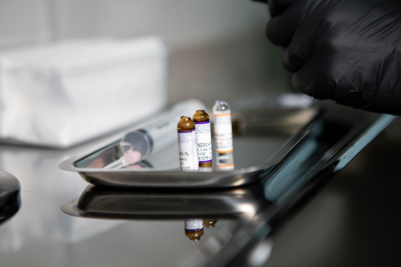 Frascos de produtos médicos e uma seringa sobre uma bandeja metálica em ambiente clínico