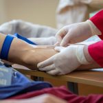 Profissional de saúde coleta sangue do braço de um doador em ambiente clínico.