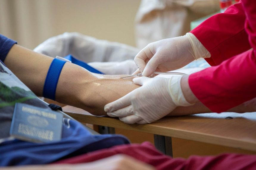 Profissional de saúde coleta sangue do braço de um doador em ambiente clínico.