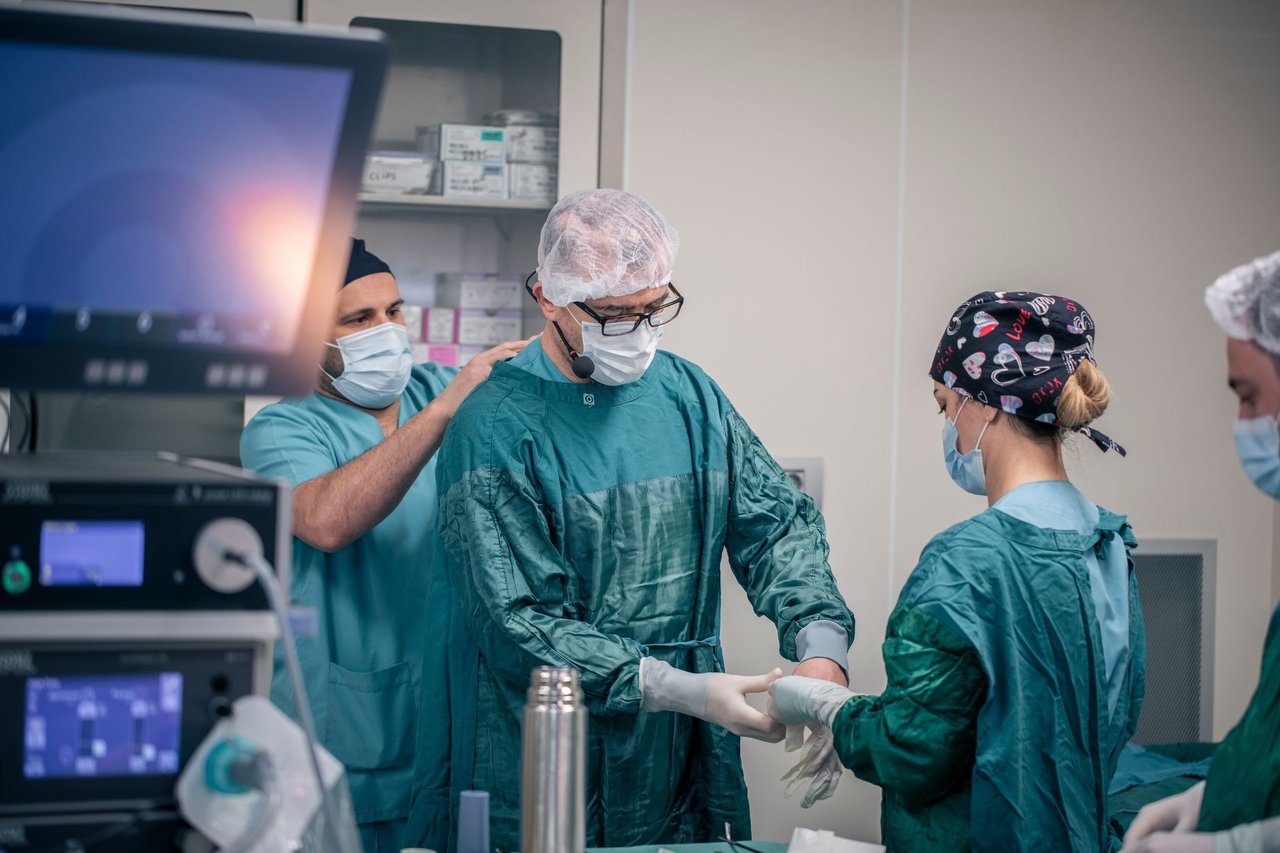 Equipe de profissionais de saúde se prepara para uma cirurgia em uma sala de operações, usando roupas e equipamentos de proteção.