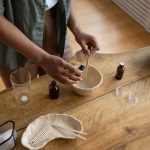 Mãos preparando artesanalmente um bálsamo labial em um ambiente interno de produção.