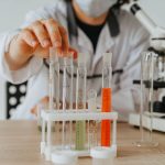 Cientista de jaleco realiza experimento com tubos de ensaio e microscópio em um laboratório.