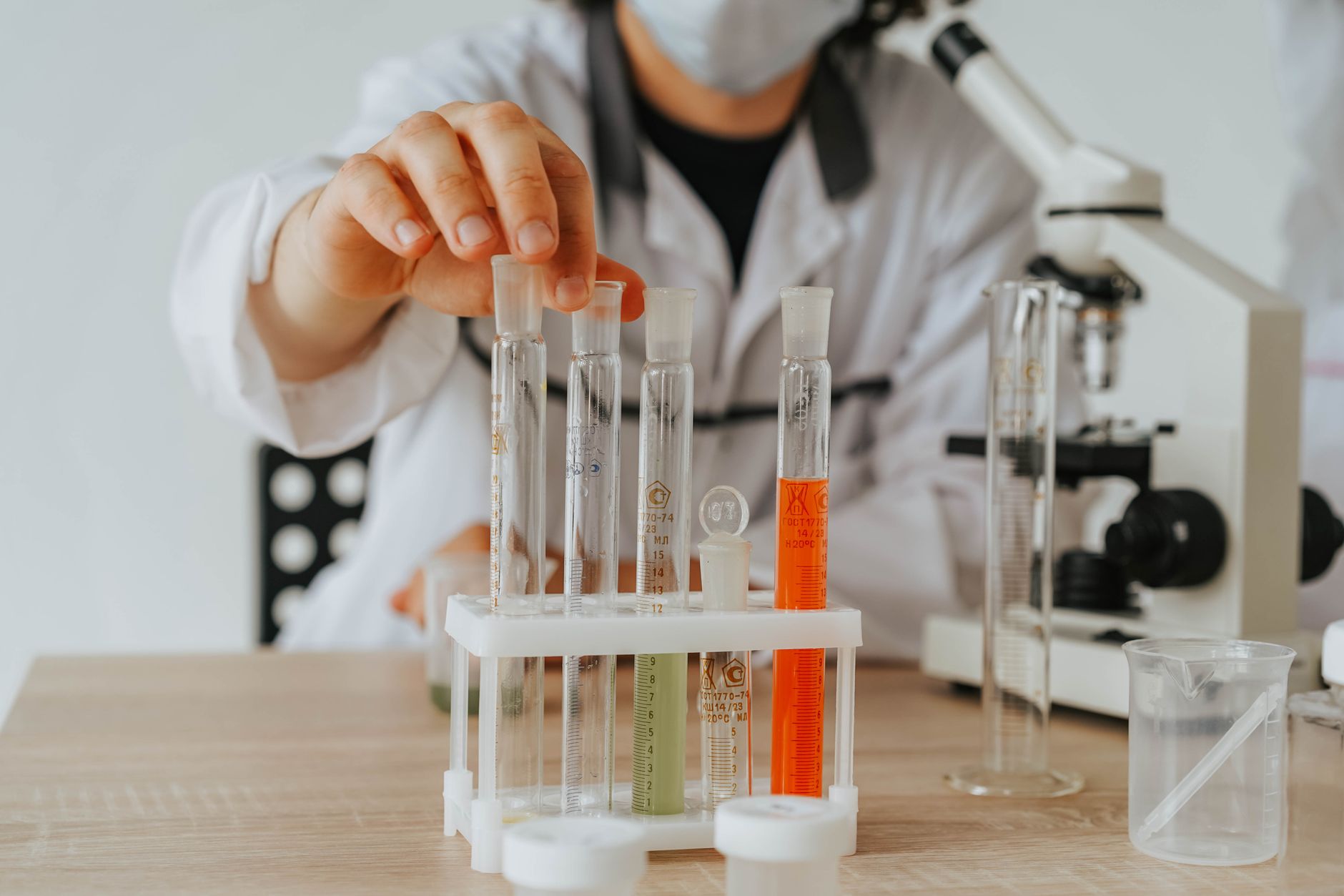 Cientista de jaleco realiza experimento com tubos de ensaio e microscópio em um laboratório.